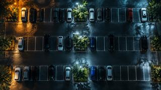 A parking lot seen from directly above, rows of parked cars between painted stalls.